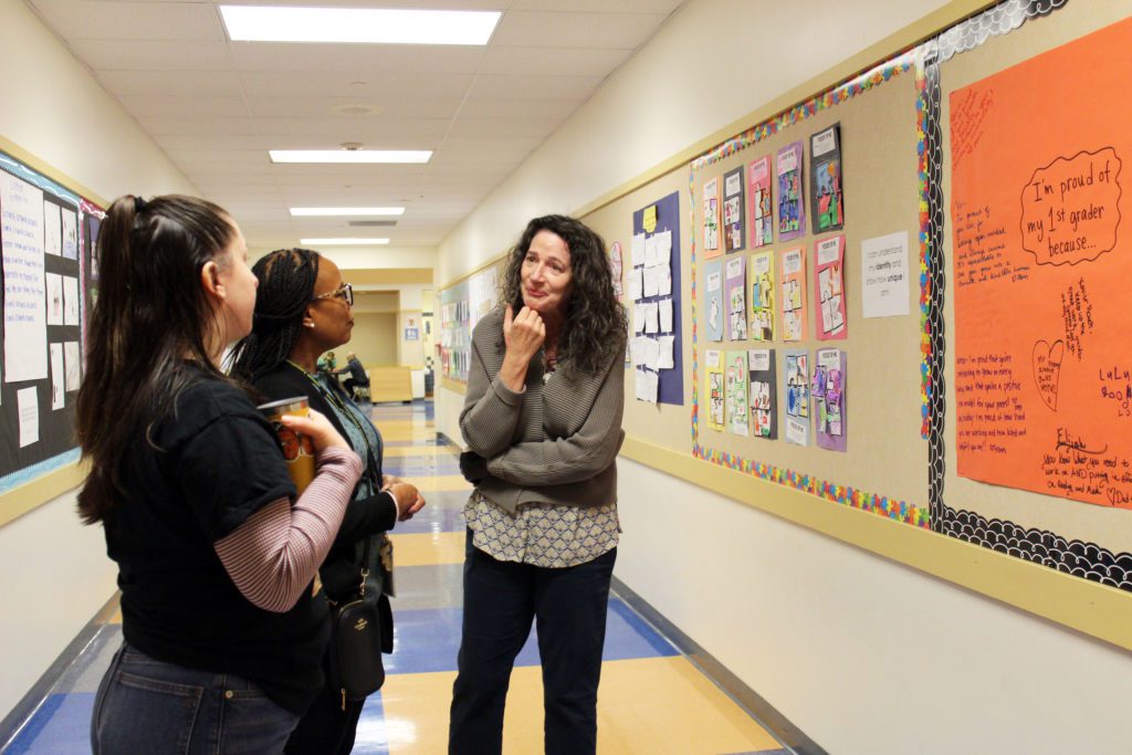 One CEL field expert, a school principal and one teacher leader discussing in a school hallway full of student work